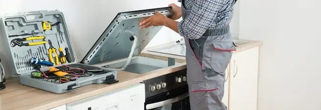Cooktop repair technician lifting a built-in stovetop for service in Akron, OH