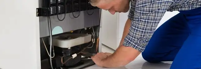 Refrigerator repair technician servicing the compressor and condenser area in Akron, OH