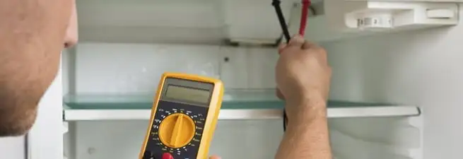 Refrigerator repair technician testing electrical components with a multimeter in Akron, OH