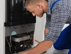 Refrigerator repair technician servicing the compressor and condenser area in Akron, OH